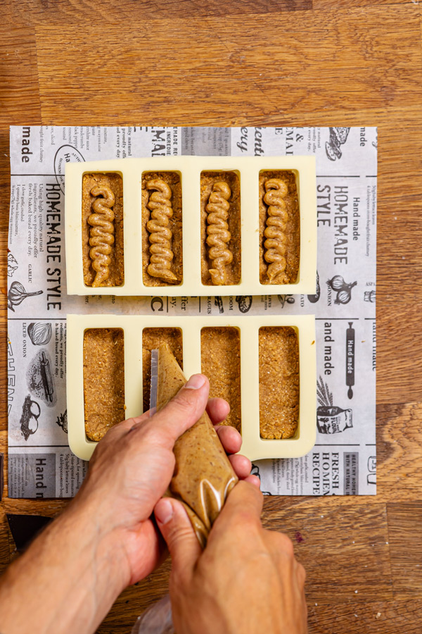 snickers creme wird mit einem spritzbeutel in eine riegel silikonform gedrueckt von oben auf holztisch