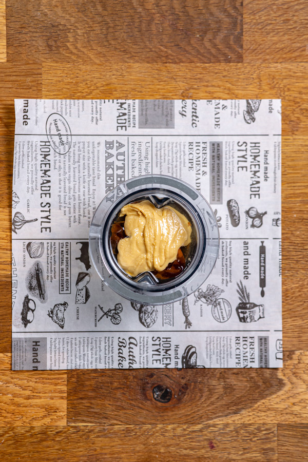 zutaten fuer creme fuer gesundes snickers in einem mixbehaelter von oben auf einem holztisch auf weissem backpapier