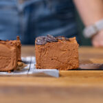 ein herausgeschnittenes stueck brownie ohne mehl auf einem holztisch frontal aufgenommen