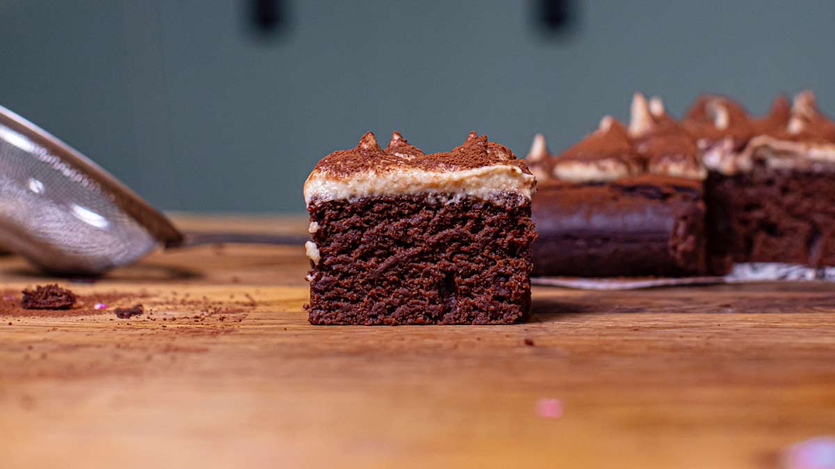 ein stueck gesundes tiramisu mit restlichem tiramisu im hintergrund auf einem holztisch von vorne