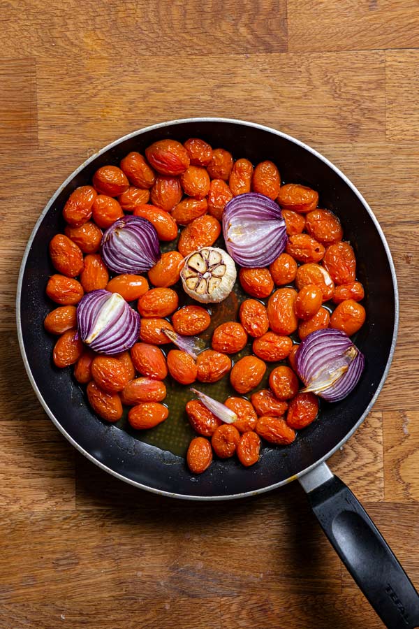 geroestete tomate mit zwiebeln und knoblauch in einer schwarzen pfanne von oben auf einem holztisch