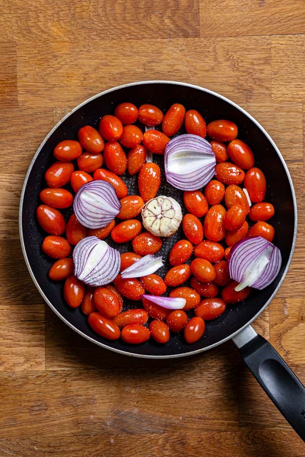 frische tomaten mit zwiebeln und knoblauch in einer schwarzen pfanne von oben auf einem holztisch