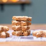 mehrere zimtsterne ohne zucker von vorne in mehrere tuerme gestapelt auf einem weissen backpapier auf einer holzunterlage