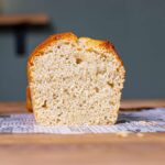 veganer zitronenkuchen angeschnitten von vorne auf einem holztisch mit dekoration