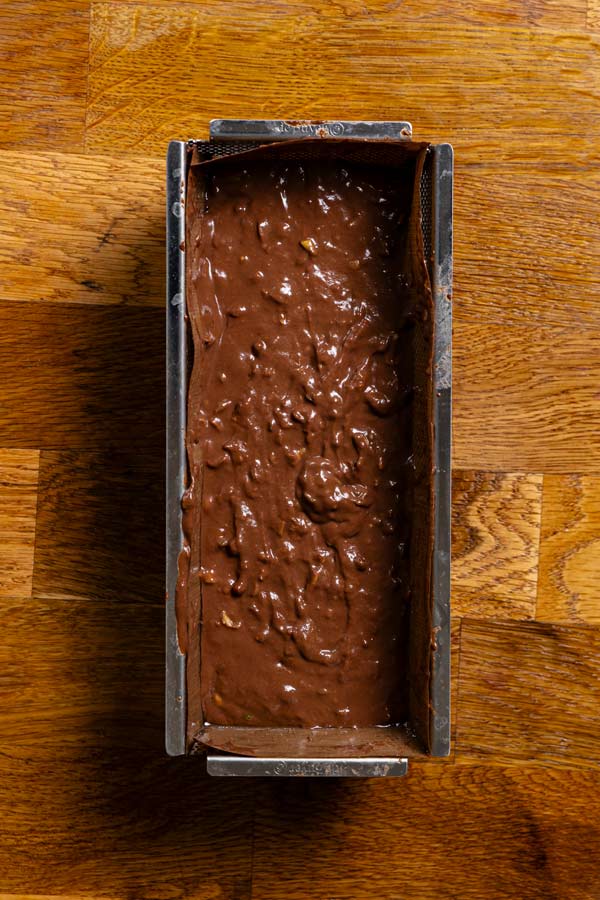 roher teig fuer kuchen mit zucchini in einer kastenform von oben auf einem holztisch