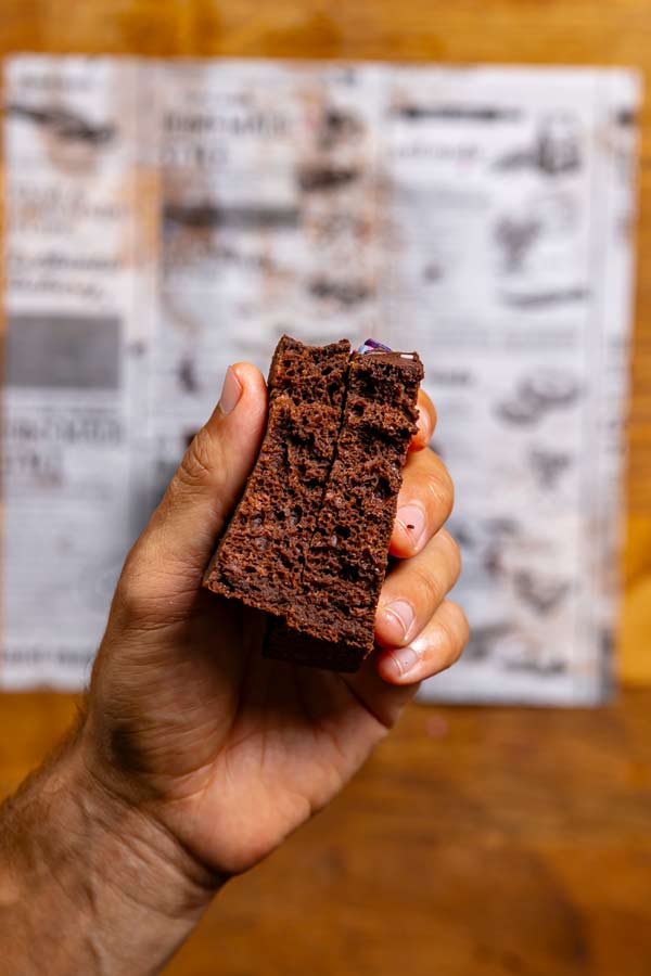 aufgebrochenes stueck kuchen mit zucchini in einer hand von oben über weissem backpapier