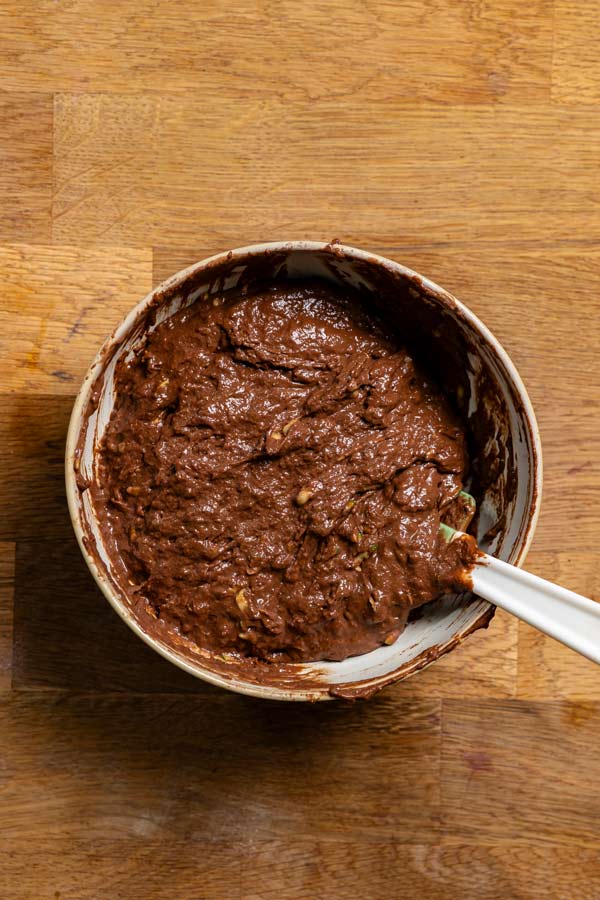 fertig vermengter teig fuer kuchen mit zucchini von oben in einer schuessel auf einem holztisch