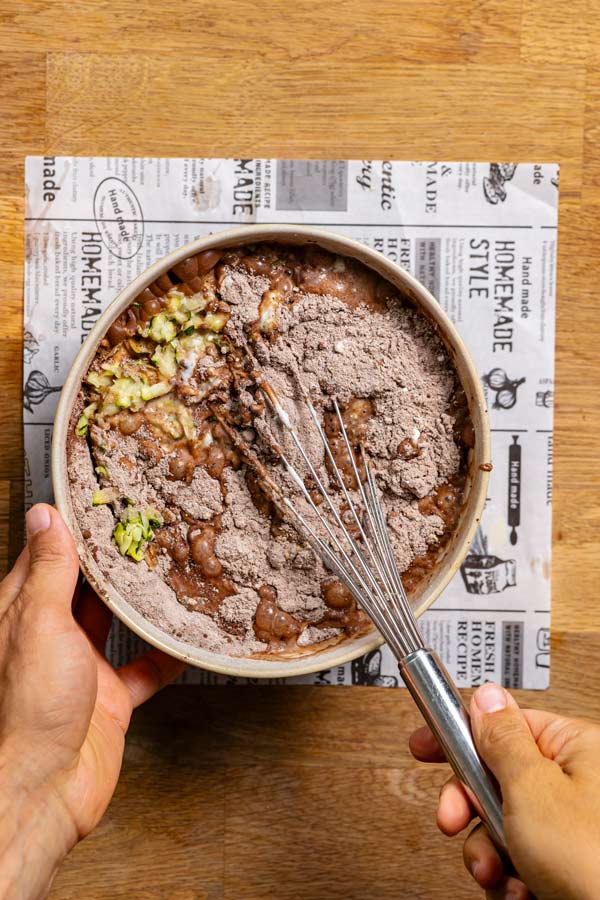 alle zutaten fuer kuchen mit zucchini in einer schuessel von oben mit zwei haenden und schneebesen