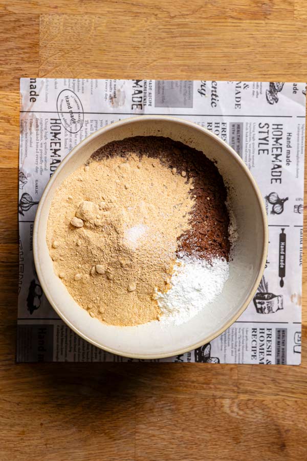 trockene zutaten fuer kuchen mit zucchini in einer weissen schuessel von oben auf holztisch