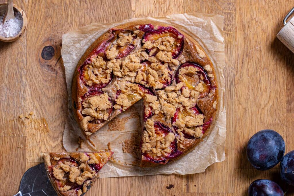 veganer pflaumenkuchen rund mit streuseln von oben auf holztisch angeschnitten