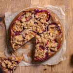 veganer pflaumenkuchen rund mit streuseln von oben auf holztisch angeschnitten