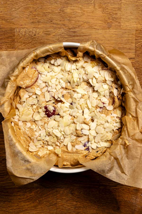 roher teig fuer kuchen mit zwetschgen in einer springform mit mandeln dekoriert