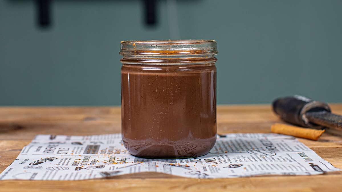 heisse schokolade in einem glas von vorne auf einem holztisch auf einem weissen backpapier