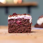 ein stueck schwarzwälder kirschtorte von vorne auf einem holztisch mit unscharfen stuecken im hintergrund