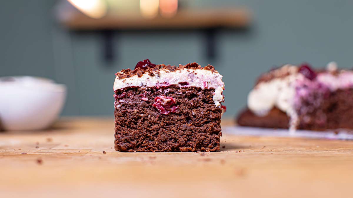 ein stueck schwarzwälder kirschtorte von vorne auf einem holztisch mit unscharfen stuecken im hintergrund